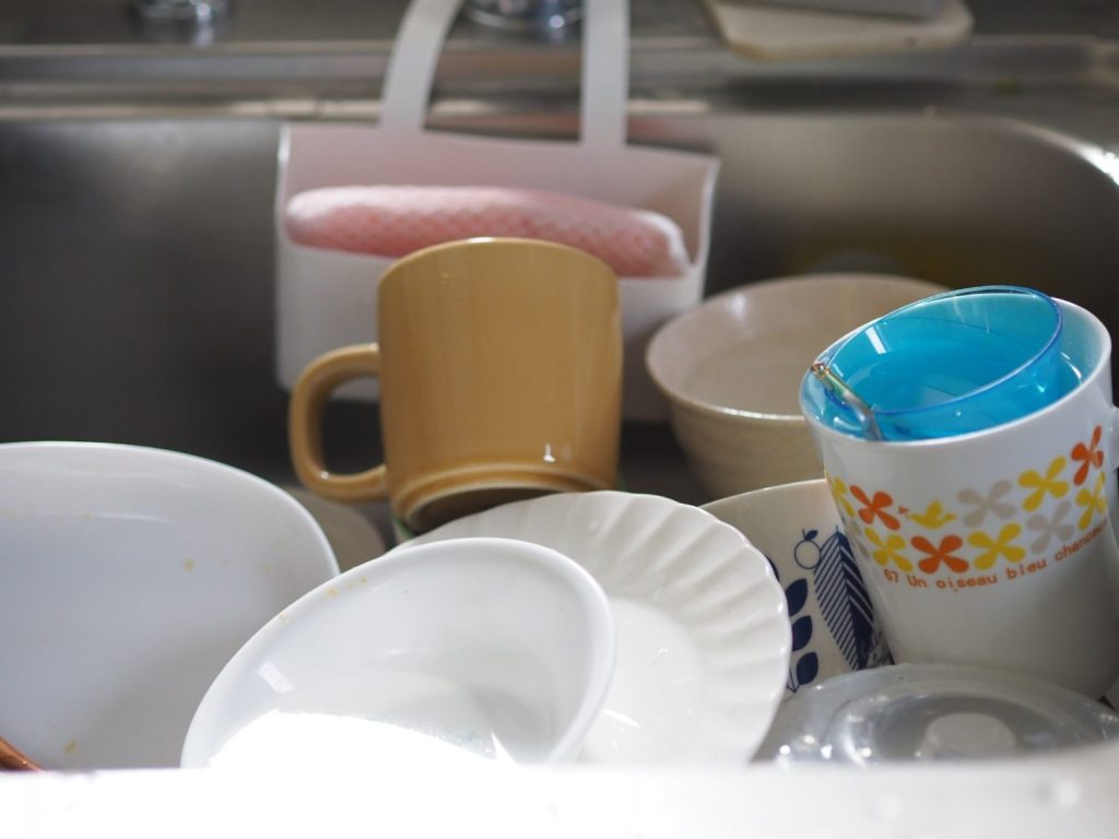 シンクの中に積み上げられた食器。食器洗いに時間がかかるため後回しにしているイメージ