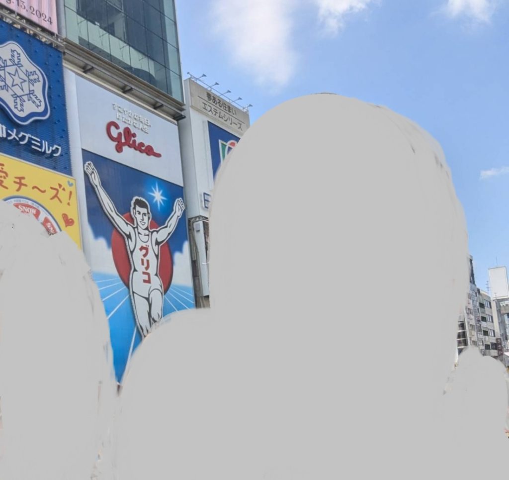 道頓堀の昼間の写真。手前に塗りつぶされた人物が写っており、その奥にグリコの看板が見える。