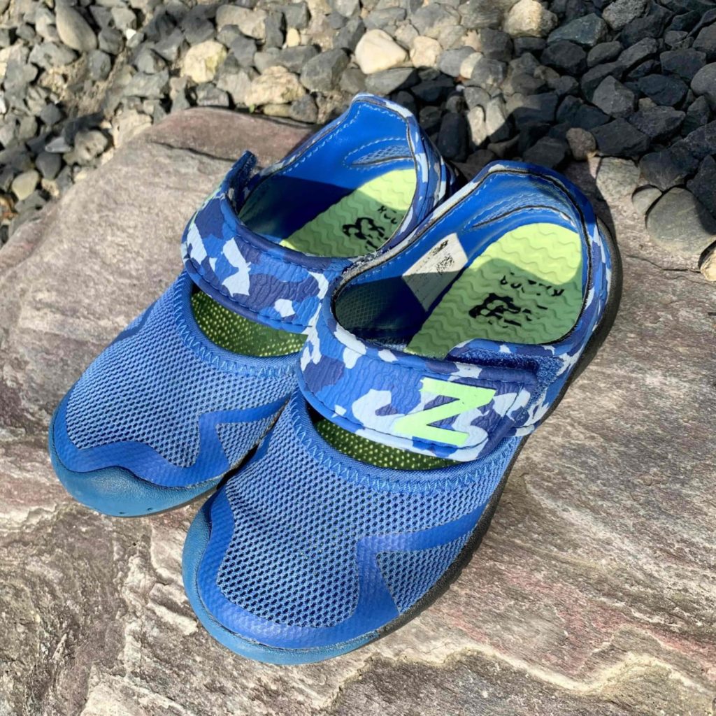 川岸の岩の上に置かれた青い子ども用ウォーターシューズ