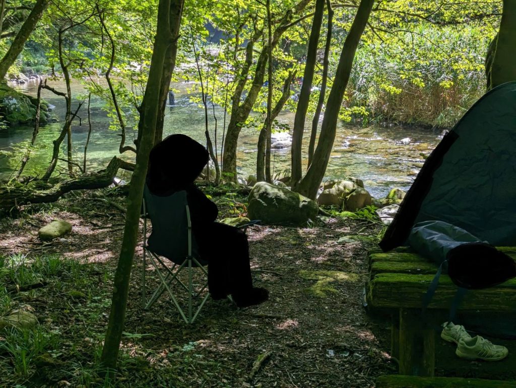 川岸のキャンプ椅子に座り、木の俣渓谷の水面を見つめる人物の後ろ姿