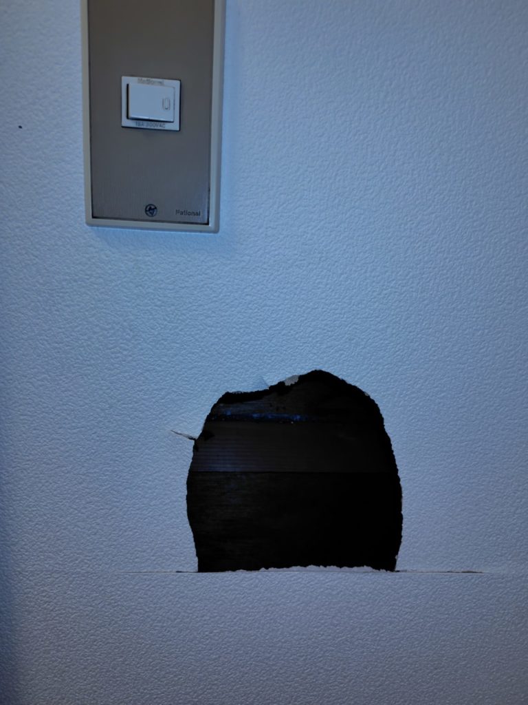 スイッチパネルの斜め下の白い壁に大きな穴が開いている様子