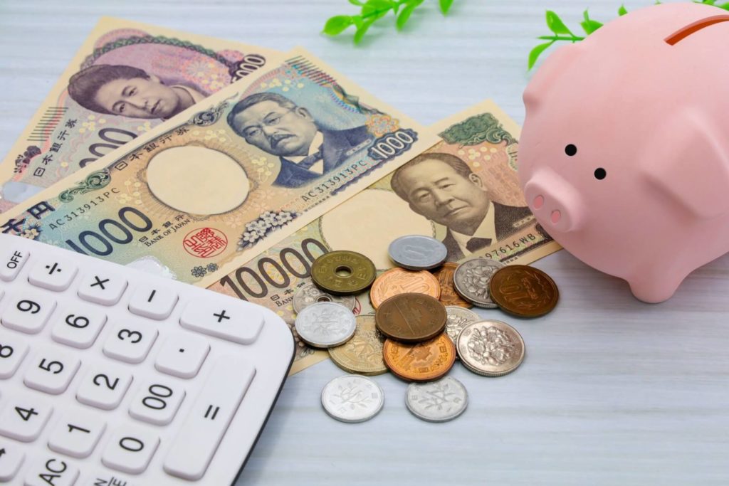 豚の貯金箱と小銭、紙幣、電卓が置いてある。発達障害の人が受けられるお金に関するセーフティーネットのイメージ